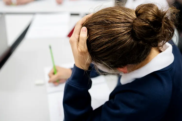 A teenager sitting calmly at a desk surrounded by study books