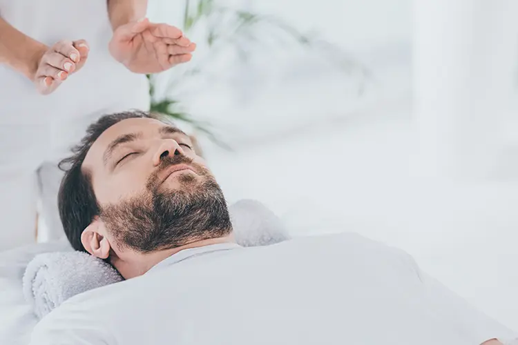 A reiki practitioner's hands positioned gently above a client lying on a treatment table